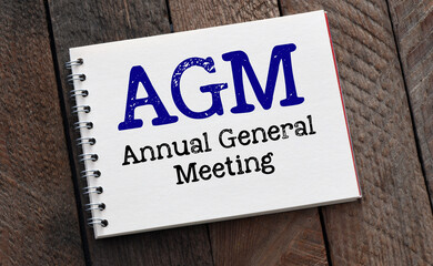 AGM Annual General Meeting words in notebook and wooden background.