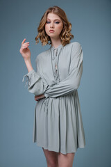 High fashion photo of a beautiful elegant young woman in pretty soft blue gray dress posing on blue background. Slim figure. Studio shot. Monochrome