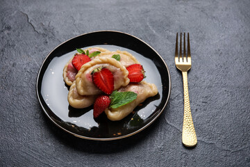 Plate with delicious strawberry dumplings on dark background