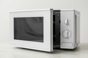 Fototapeta premium Microwave oven with opened door on table against light background