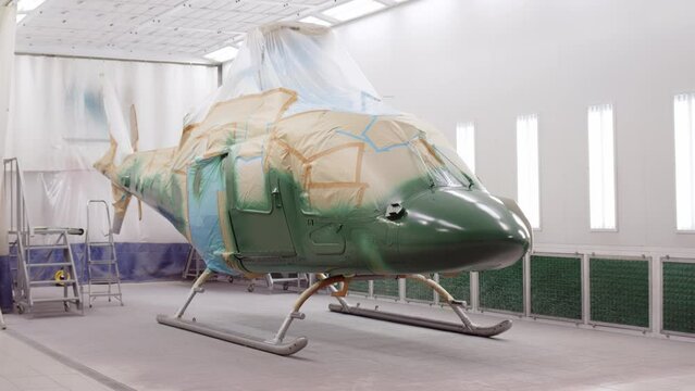 military or civilian helicopter stands in spray booth and is painted khaki green. aircraft is being repaired at docks. business helicopter painted and recolored. Military equipment for maintenance.