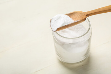 Jar and spoon with baking soda on white wooden background