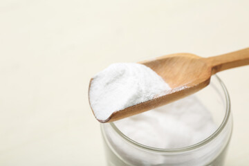 Jar and spoon with baking soda on white wooden background, closeup