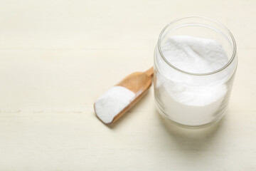 Jar and spoon with baking soda on white wooden background
