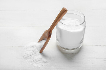 Jar and spoon with baking soda on white wooden background