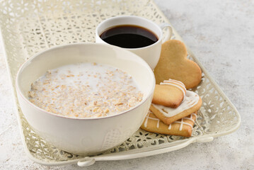 Bowl of tasty oatmeal, cookies and cup with coffee on light background