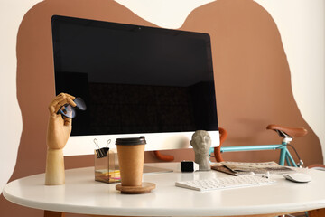 Modern computer, different gadgets, paper cup with coffee and stylish decor on table near color wall