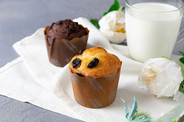 Cupcakes with raisin, chocolate and glass of milk and flowers on background.