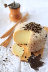  Piece of Pecorino cheese with black pepper on wooden cutting board with wooden cutlery, rustic styling on light background, Mediterranean diet concept, mature cheeses, Italian food.