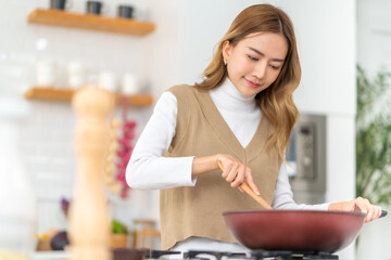Beautiful Asian woman enjoy cooking healthy food pasta and salmon steak on cooking pan in the kitchen at home. Happy female having dinner party meeting celebration with friends on holiday vacation