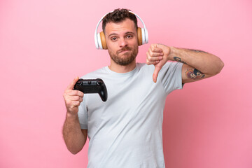 Young Brazilian man playing with video game controller isolated on pink background showing thumb...