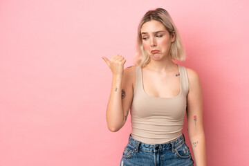 Young caucasian woman isolated on pink background unhappy and pointing to the side