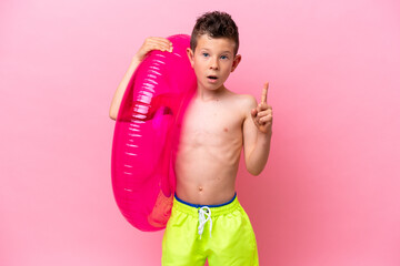 Little caucasian boy holding a inflatable donut isolated on pink background thinking an idea pointing the finger up