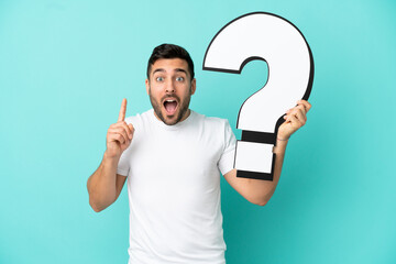 Young handsome caucasian man isolated on blue background holding a question mark icon