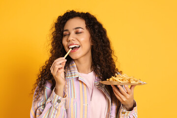 African American woman eating French fries on yellow background - Powered by Adobe