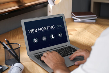 Web hosting service. Man working on laptop at wooden table, closeup