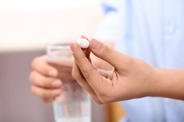 Obraz na płótnie Canvas Calcium supplement. Woman holding pill and glass of water on blurred background, closeup