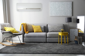Modern air conditioner on light grey wall in living room with stylish furniture