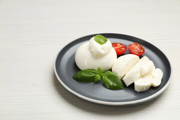 Delicious burrata cheese with basil and cut tomato on white wooden table