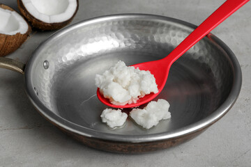 Frying pan with coconut oil and spoon on light grey table