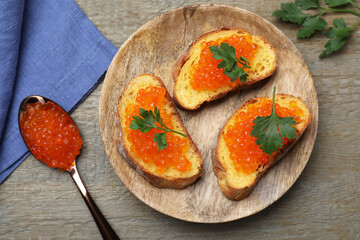 Delicious red caviar sandwiches with parsley on wooden table, flat lay