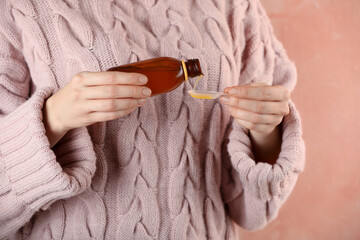 Woman pouring cough syrup into spoon on pink background, closeup