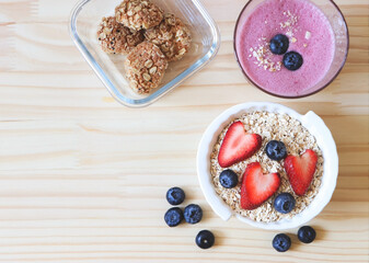 flat lay of  breakfast with oat or granola in white bowl, fresh blueberries, strawberries, a  glass of blueberry smoothie and oat cookies  on wooden table. Healthy breakfast concept.
