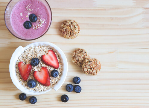 flat lay of  breakfast with oat or granola in white bowl, fresh blueberries, strawberries, a  glass of blueberry smoothie and oat cookies  on wooden table. Healthy breakfast concept.