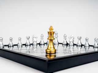 The Golden king chess piece standing on chessboard corner in front of many silver chess pieces on...