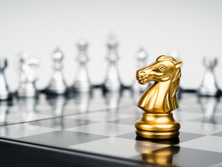 The golden horse, knight chess piece stand alone in front of silver chess pieces on chessboard on white background. Leadership, fighter, surviver, competition, and business strategy concept.
