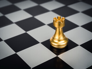 The golden rook chess piece standing alone on chess board background. Rook or the castle, the tower...