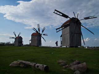 A man near three Ukrainian traditional wooden windmills against the blue sky. traditional Ukrainian history