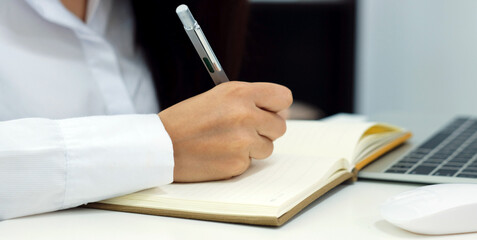 Woman hand wrting on notebook paper on table at home office