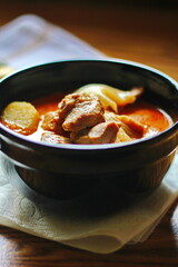 Massaman curry in black crockery served with boiled potatoes and chili on a brown wooden table.