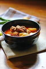 Massaman curry in black crockery served with boiled potatoes and chili on a brown wooden table.
