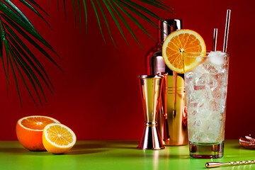 Tom Collins popular alcoholic cocktail with dry gin, syrup, lemon juice, soda, orange and ice. Bright red green summer background, negative space