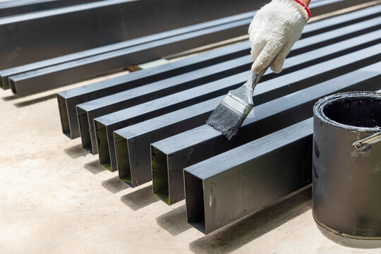 Worker painting steel post in construction site.