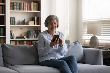 Obraz premium Cheerful senior smartphone user woman talking on video call, reading message with good happy news, laughing. Mature lady using internet app on mobile phone, shopping, getting discount, profit