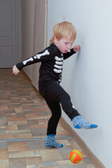 A child in a skeleton costume plays football in the hallway of the house - 504690127