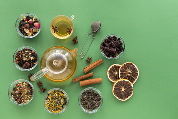 A set of different varieties of Chinese herbal and green tea in a glass dish and a kettle with hot tea on a green background. View from above. Space for text. Herbal treatment. Healthy lifestyle.