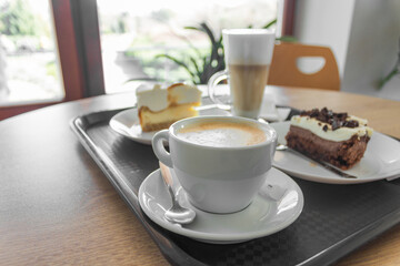 Pieces of cheesecake and chocolate cake with cups of coffee on a tray. Coffee break in the cafe.