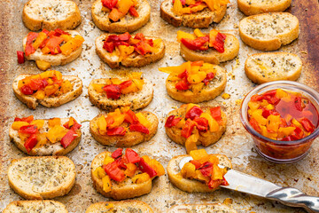 bruschetta mini toasts spread with oily gourmet red, yellow, and orange pepper topping on baking sheet 
