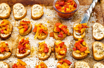 bruschetta mini toasts spread with oily gourmet red, yellow, and orange pepper topping on baking sheet 