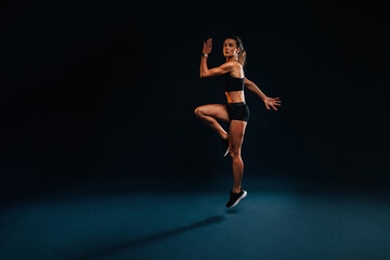 Obraz premium Female athlete jumping and stretching. Healthy woman exercising in studio warming up.