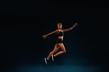 Fototapeta premium Slim woman working out on black background. Female athlete doing jumps in studio.