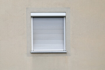 Window with closed shutters, white jalousie roll up, wall bright with frame, no person