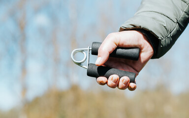 Woman using hand expander while exercising outdoors. Close-up of woman's hand squeezing carpal spring trainer