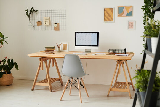 Modern home office with wooden desk, computer, planning board and abstract pictures on wall