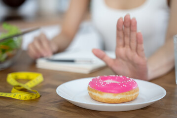 Woman on dieting for good health concept. Close up female using hand push out her favourite donut and choose salad vegetables for good health.