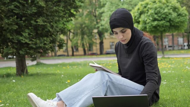 Confident islamic woman muslim girl student in hijab sitting on the grass lawn in park outdoors female teacher online mentor preparing for the lecture using laptop distant online communication.